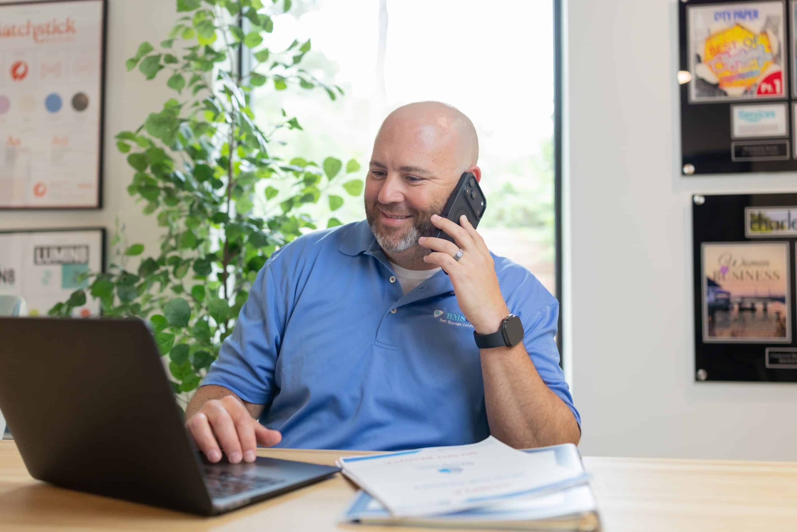 BMSGRP self-storage consultant reviewing documents on a laptop while speaking with a client by phone about self-storage investment and development.